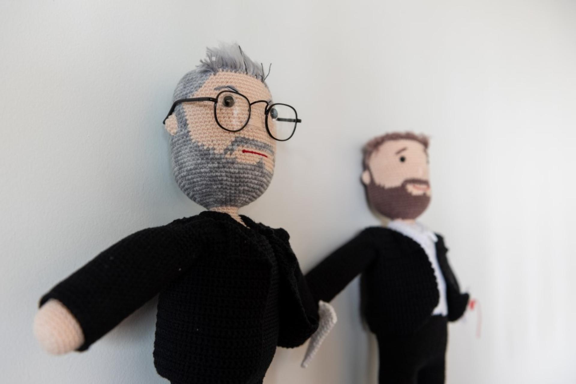 Two puppets against a wall. one with grey hair, bread and glasses and the other with brown hair and a beard