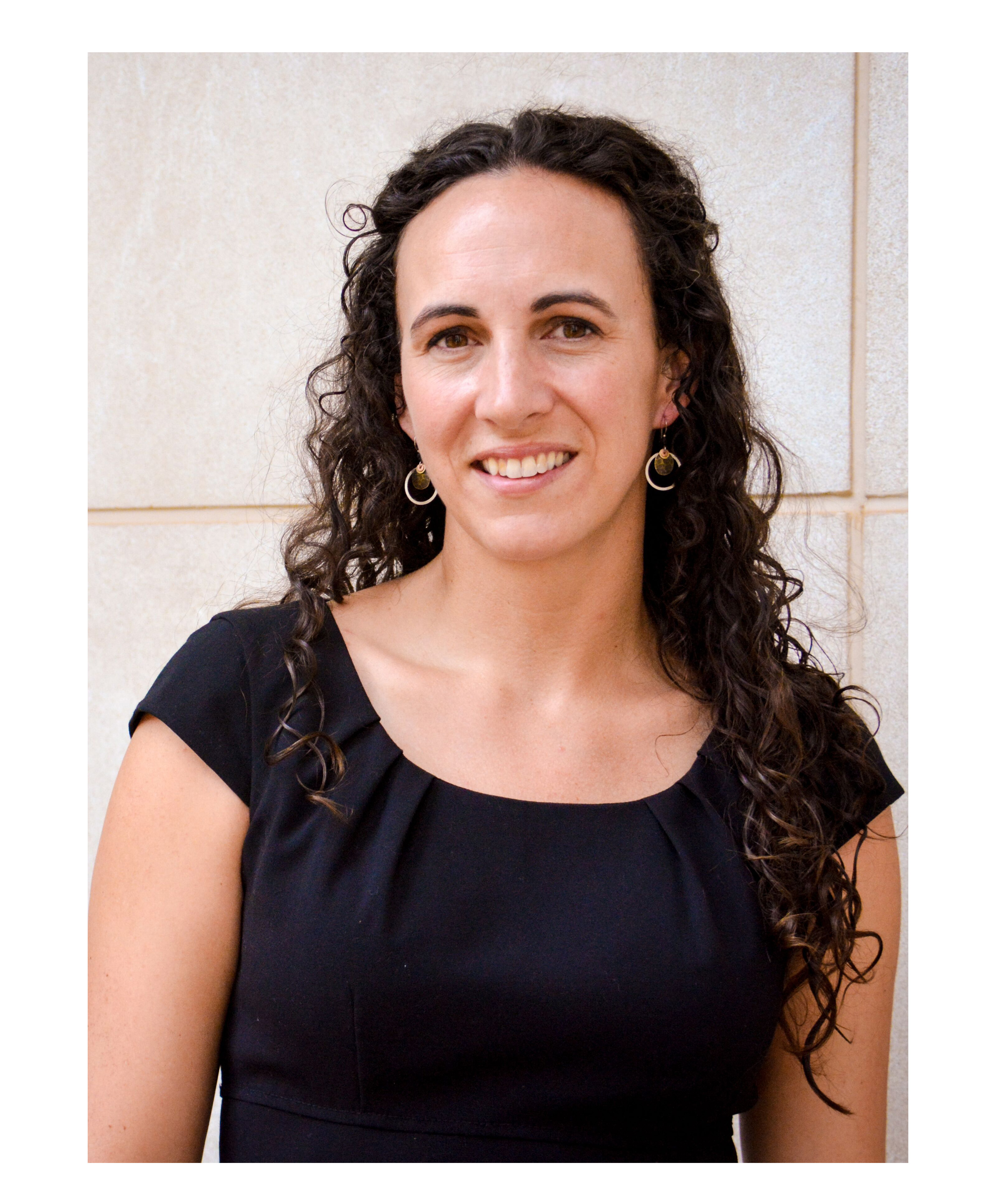 Professor Welton has dark curly hair and looks into the camera smiling.