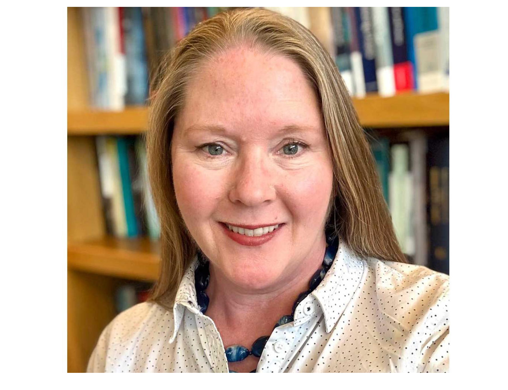 Kasey McCall-Smith has long blonde/brown hair and smiles into the camera wearing a black and white spotted shirt. 