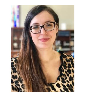 Roxana Banu sits in a sunny portrait. She has long brown hair and black glasses.