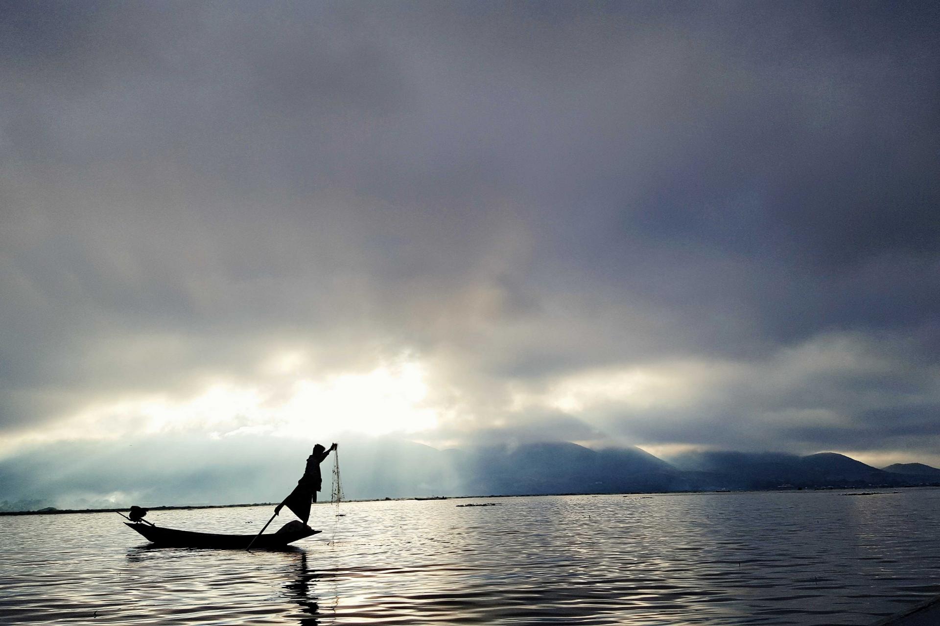 Silhouette of person on boat with clouds and sun in background