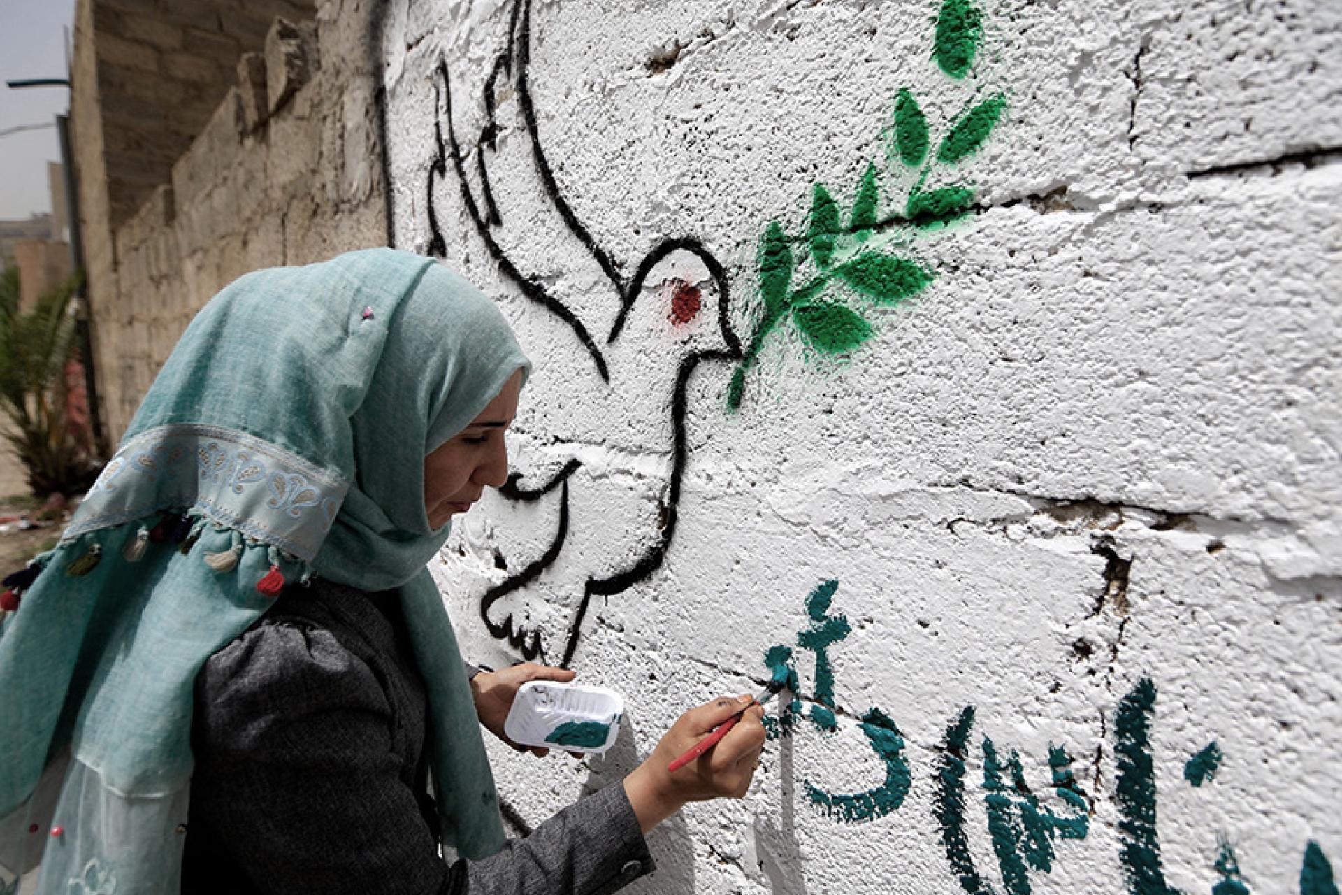 a woman painting on a wall with a white dove
