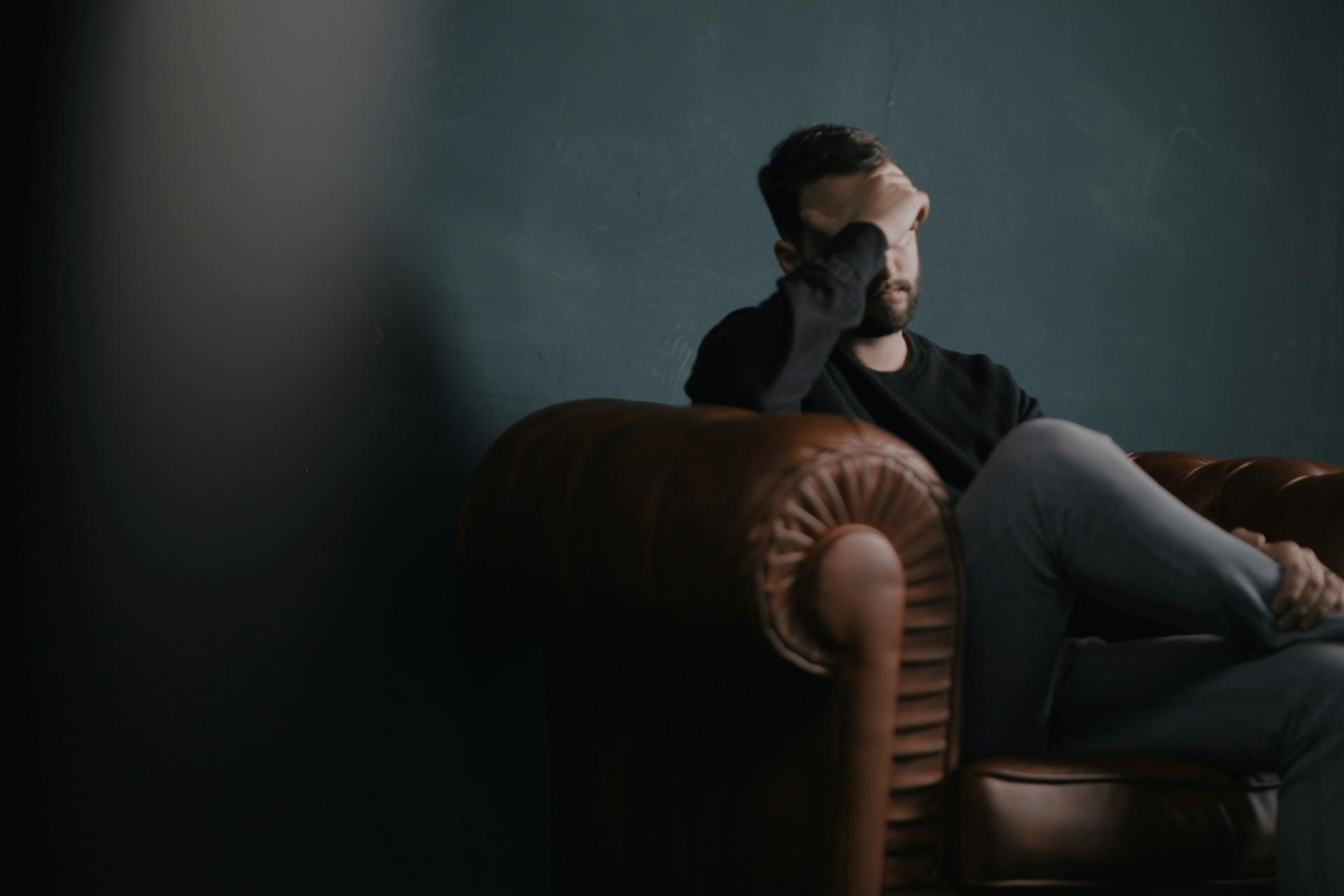 A man sitting on a couch with his hand covering his face