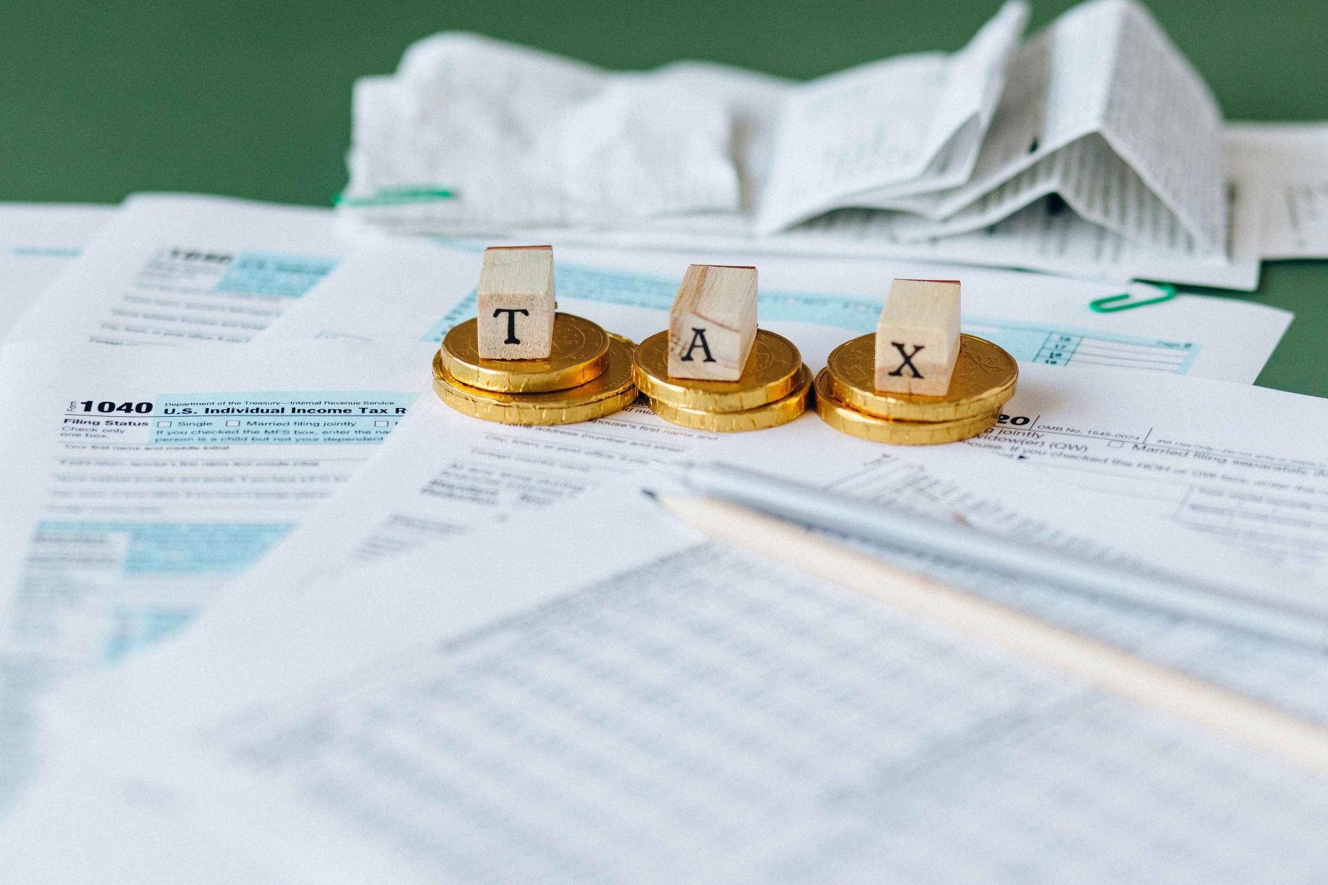 the letters T A X sitting on gold coins on top of tax paper work with receipts in the background 
