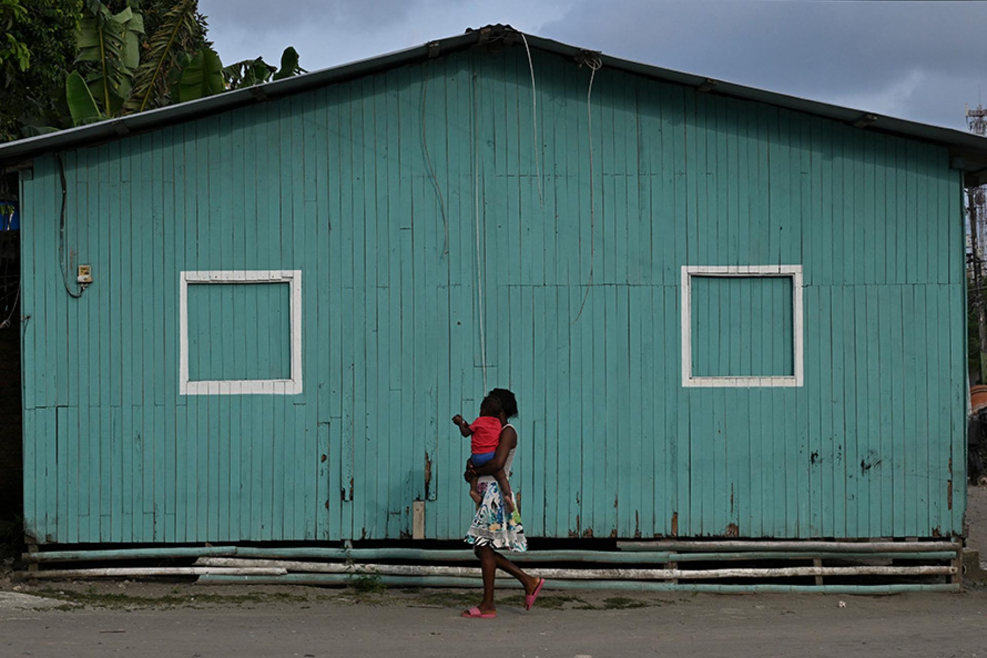 a woman walking and carrying a child with a green building in the background