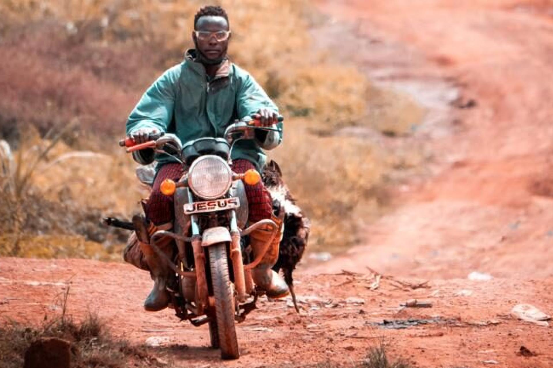 A man sits on a motorcycle in an arid environment. 